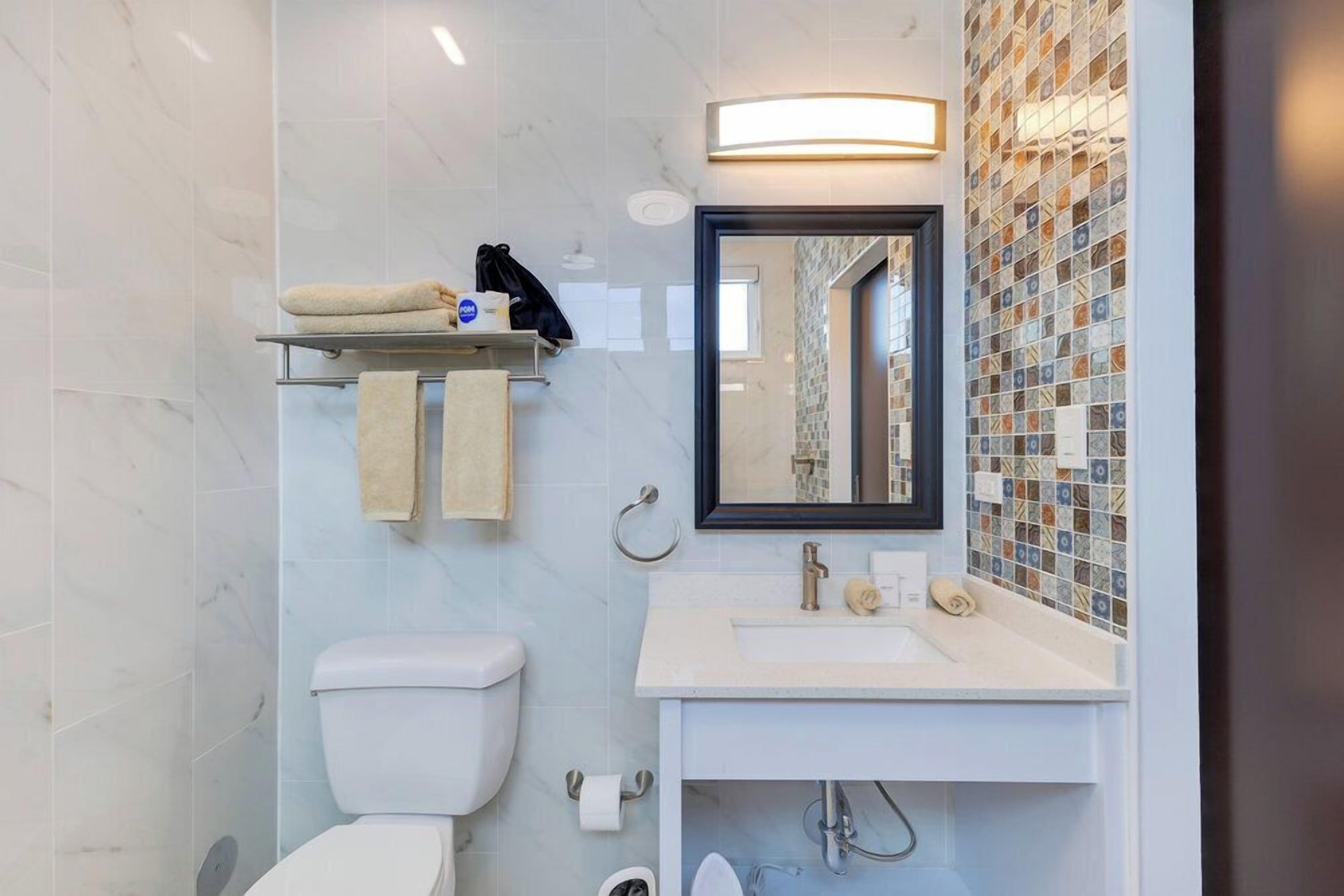 Un bagno moderno con toilette, lavandino e specchio. Asciugamani e articoli da toilette sono presenti su un ripiano a parete.
