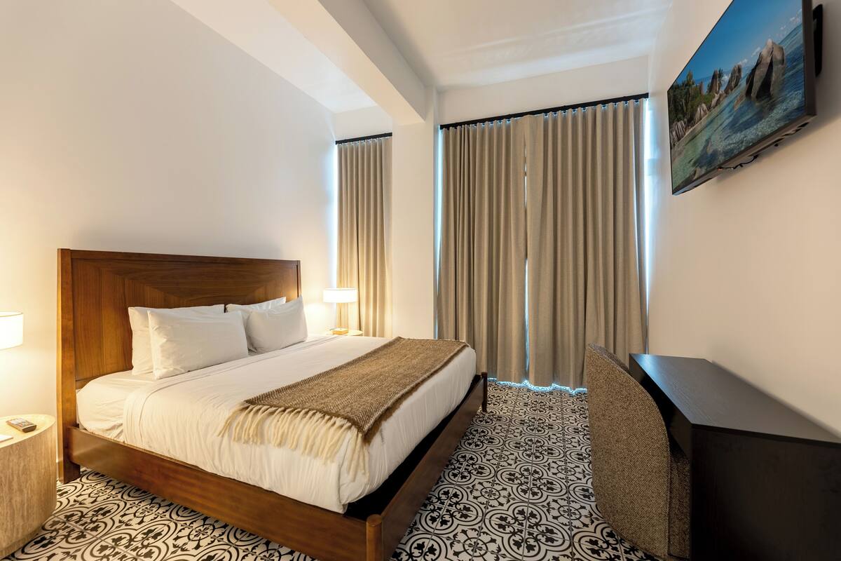 A hotel room with a wooden bed, a desk, and a large window with curtains.
