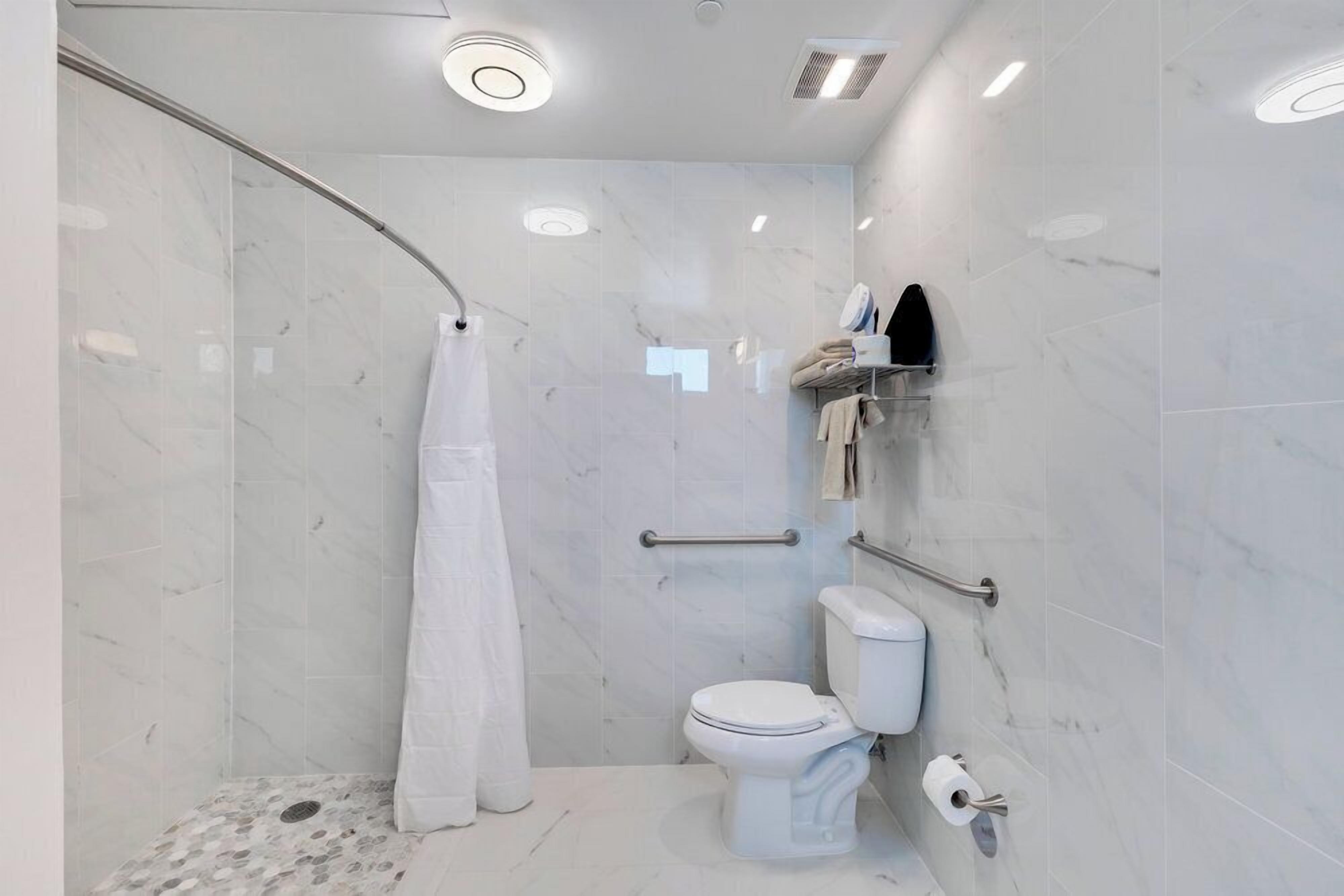 A modern bathroom with a shower, toilet, and handrails.