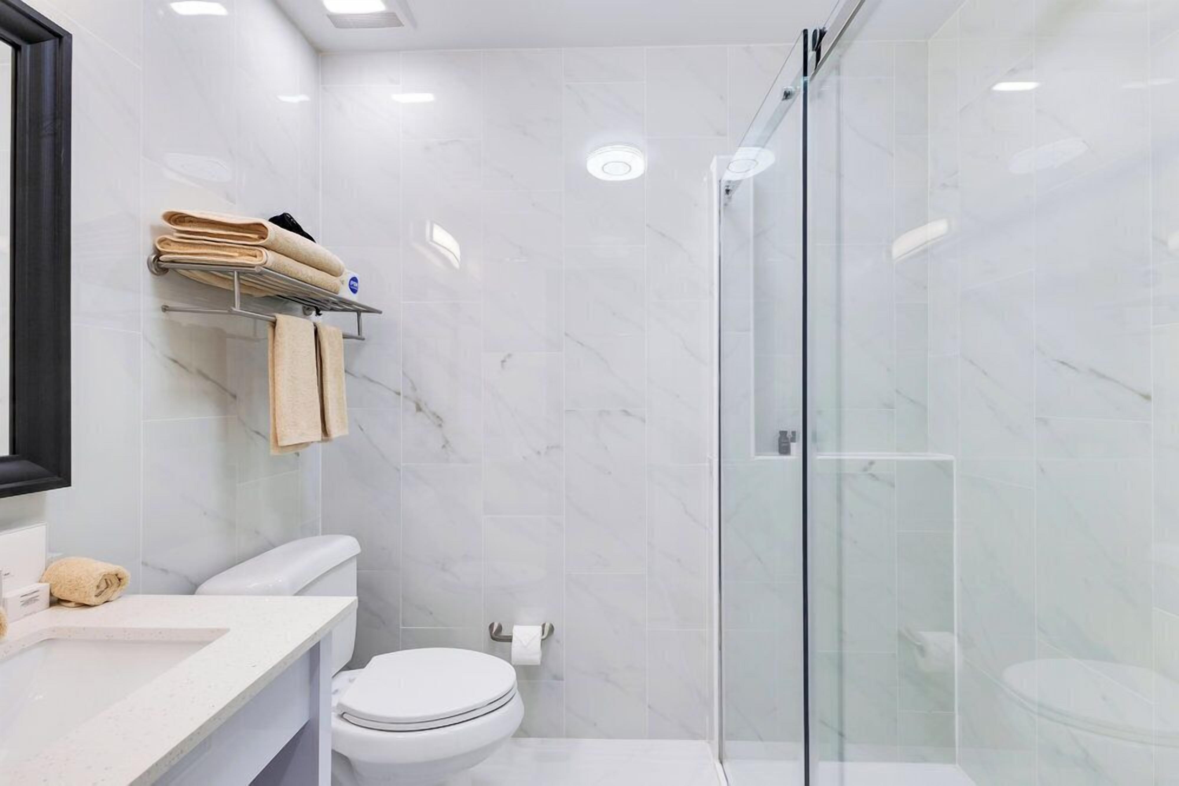 A modern bathroom with a glass-enclosed shower, a white toilet, and a vanity with a mirror and towel rack.