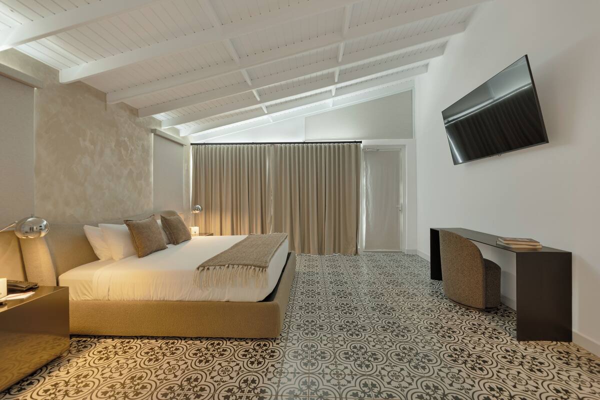 A modern hotel room with a large bed, a desk, and a TV mounted on the wall.