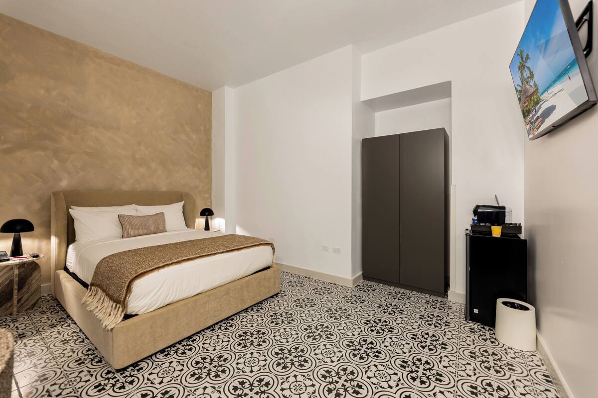 A modern hotel room with a bed, a nightstand, a wall-mounted TV, and a door.