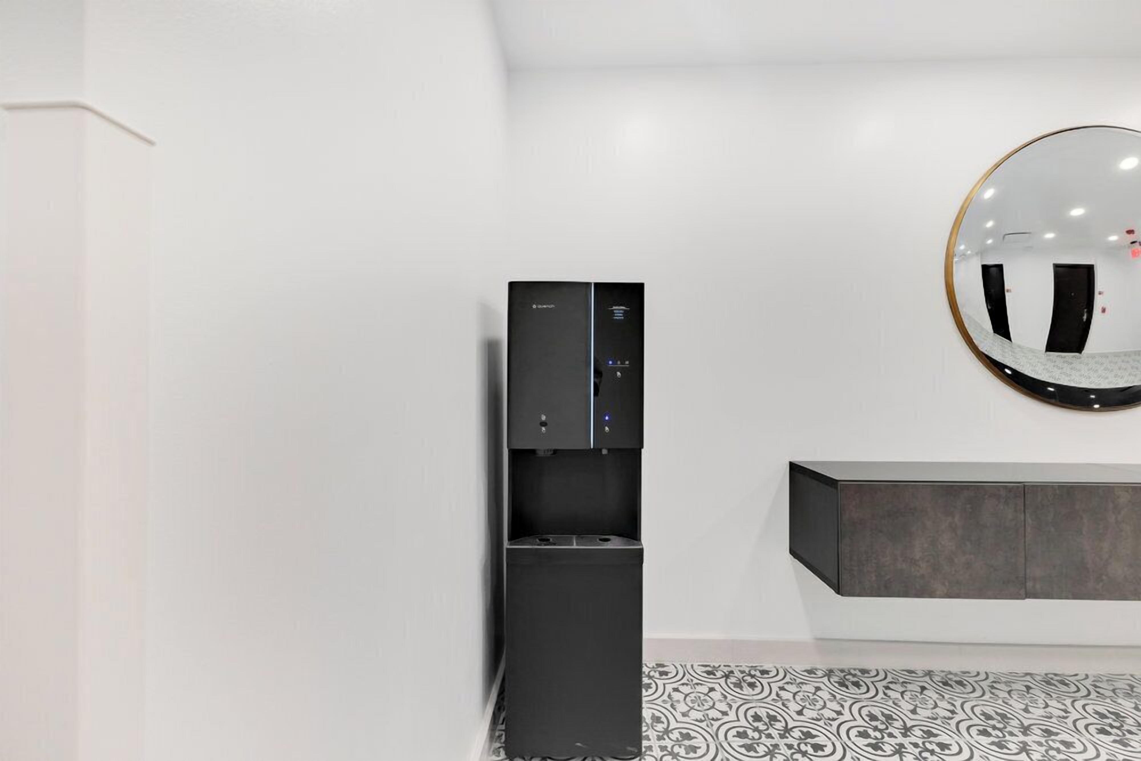 Quarto moderno com minibar preto, espelho redondo e piso estampado.