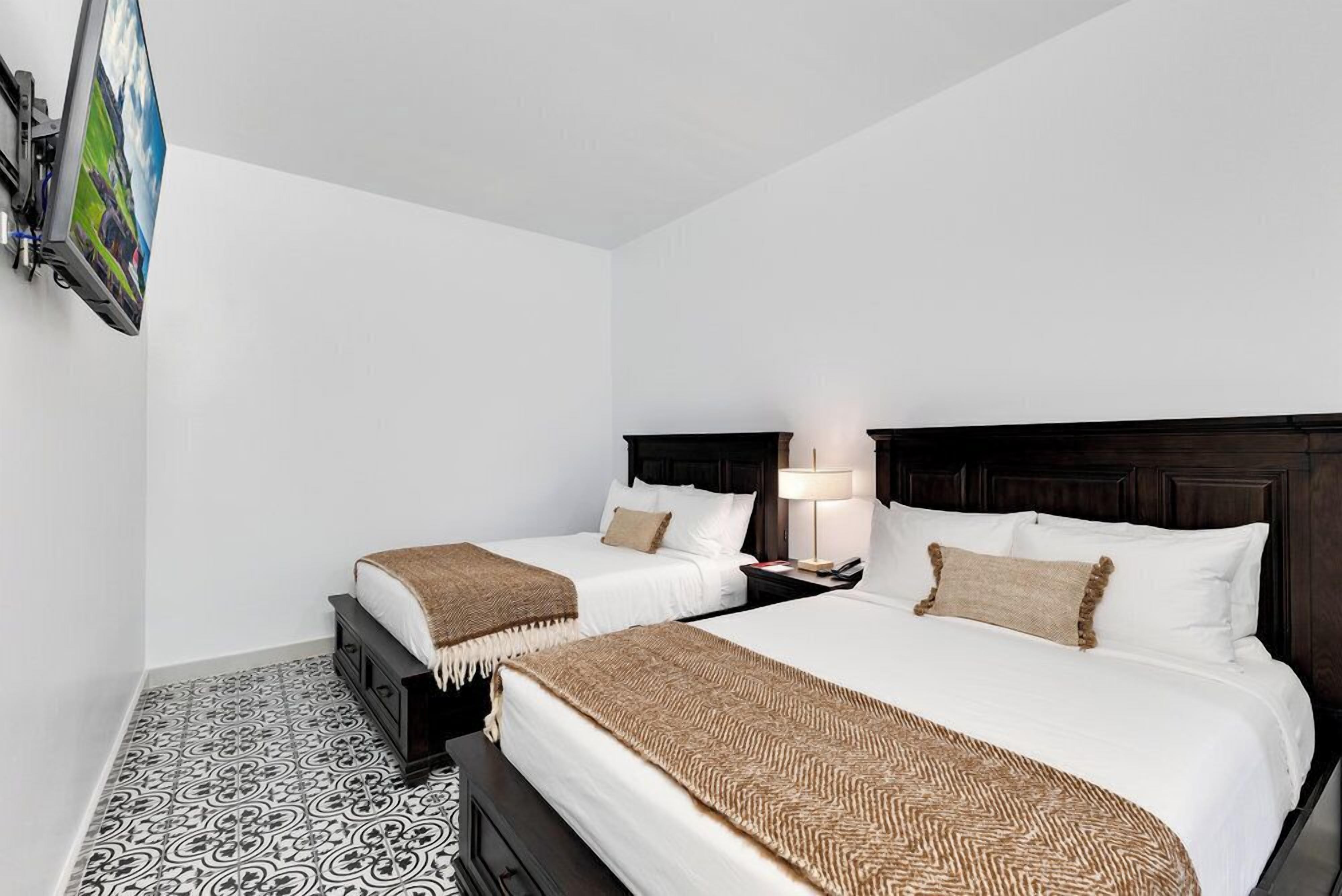 Una habitación de hotel con dos camas, un televisor montado en la pared y un suelo estampado.