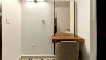 Une petite pièce avec un bureau en bois, une chaise, une lampe fixée au mur et un miroir.