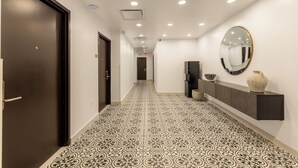 A hallway with patterned floor tiles, a dark door, a wall-mounted mirror, and a dark console with decorative items. - Hotel Milano (San Juan)