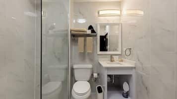 Un baño moderno con cabina de ducha de vidrio, inodoro, lavamanos con espejo y un perchero para toallas.