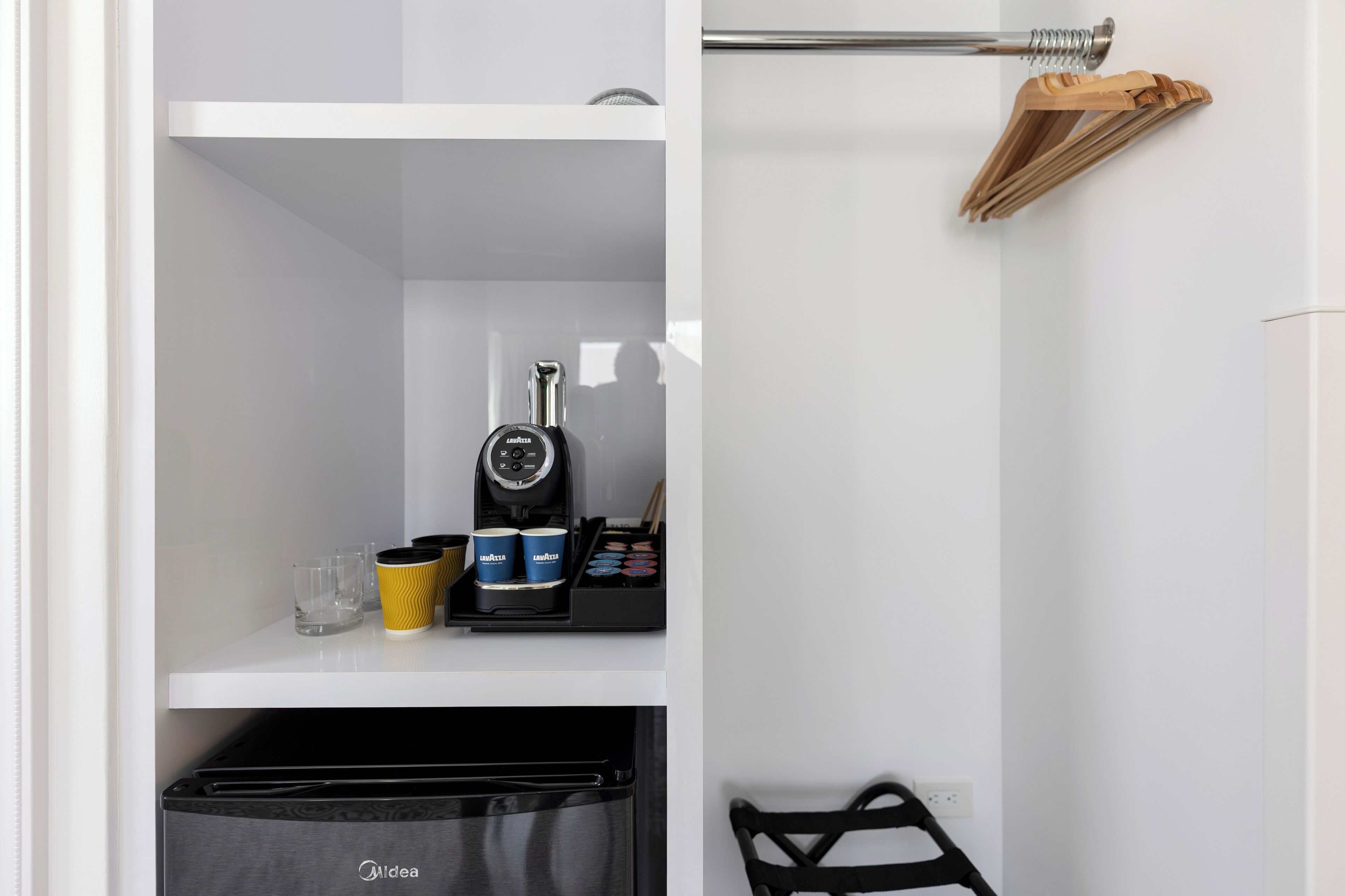 Une cuisine compacte équipée d’une machine à café, d’une bouilloire et d’un petit espace de rangement.