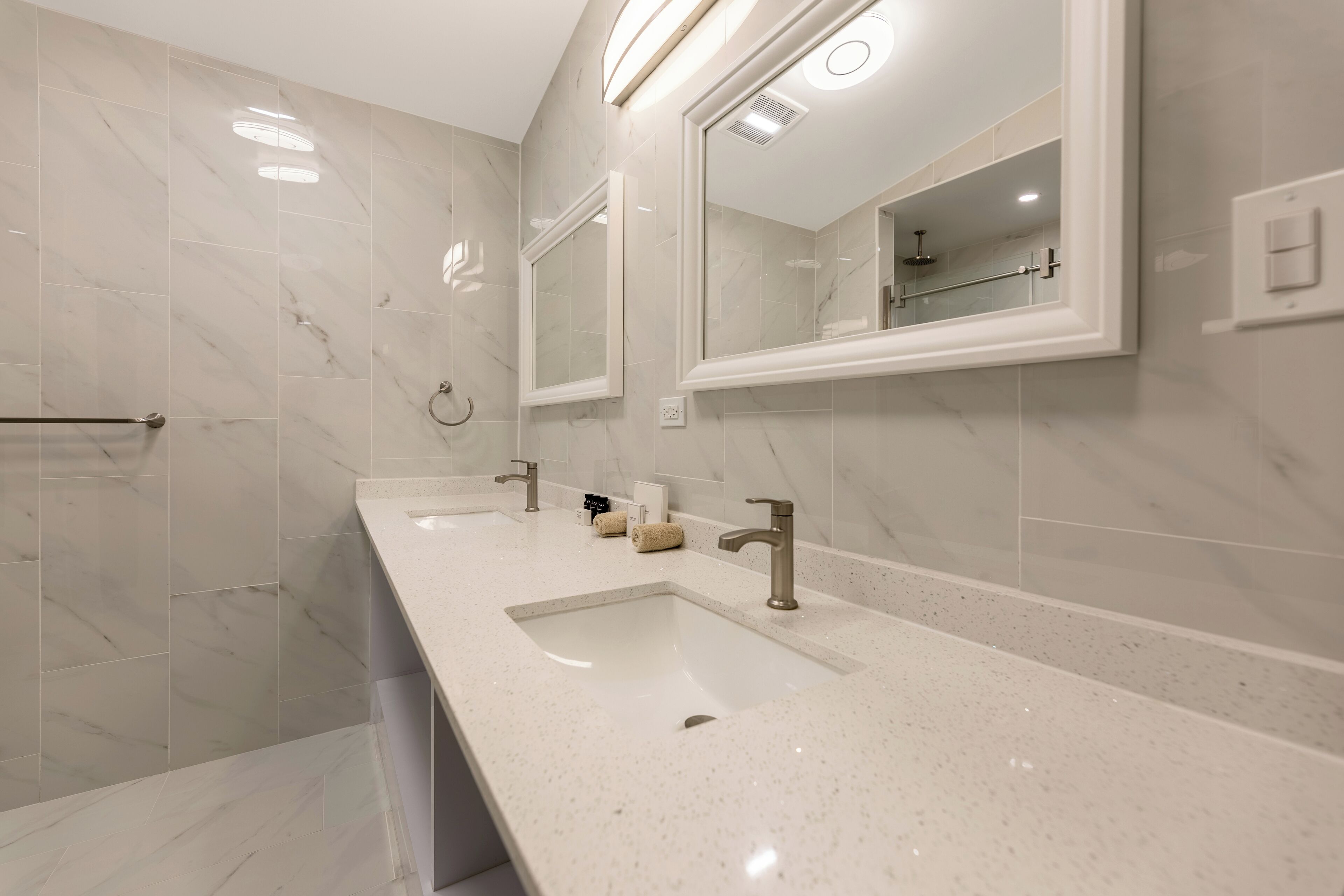 Une salle de bain moderne avec deux lavabos, un grand miroir et un espace douche.