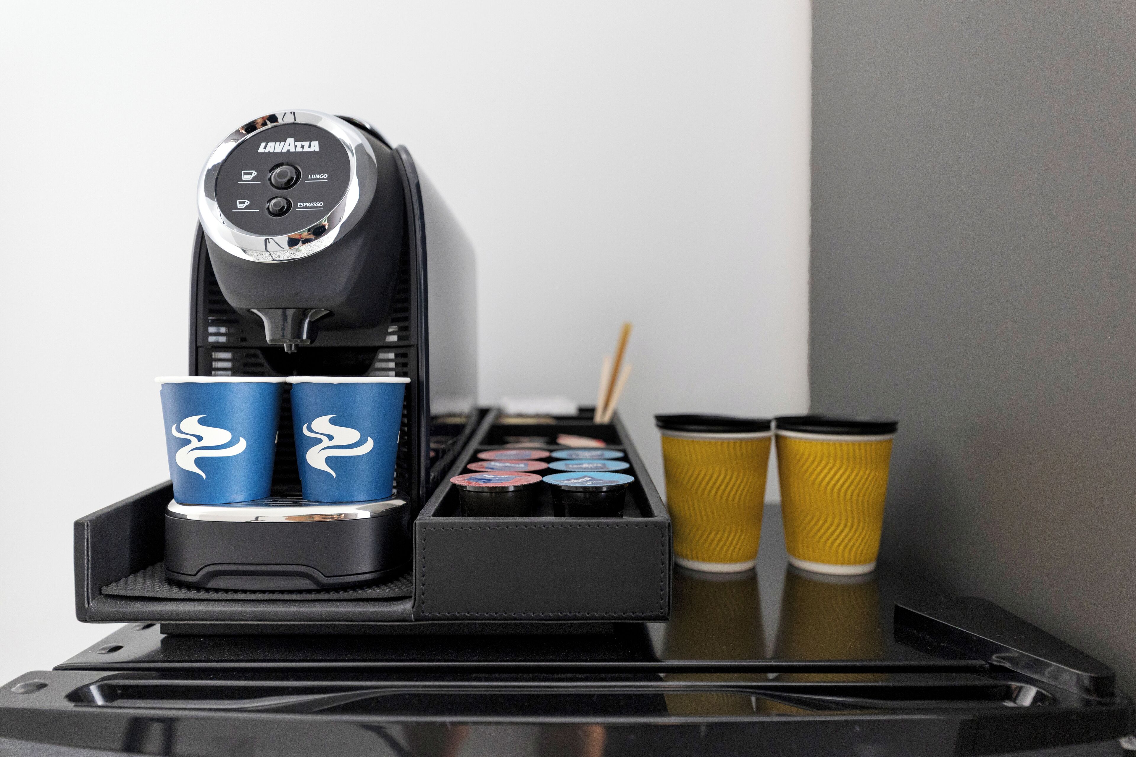 Eine Kaffeemaschine mit zwei blauen und zwei gelben Tassen auf einem Tablett.