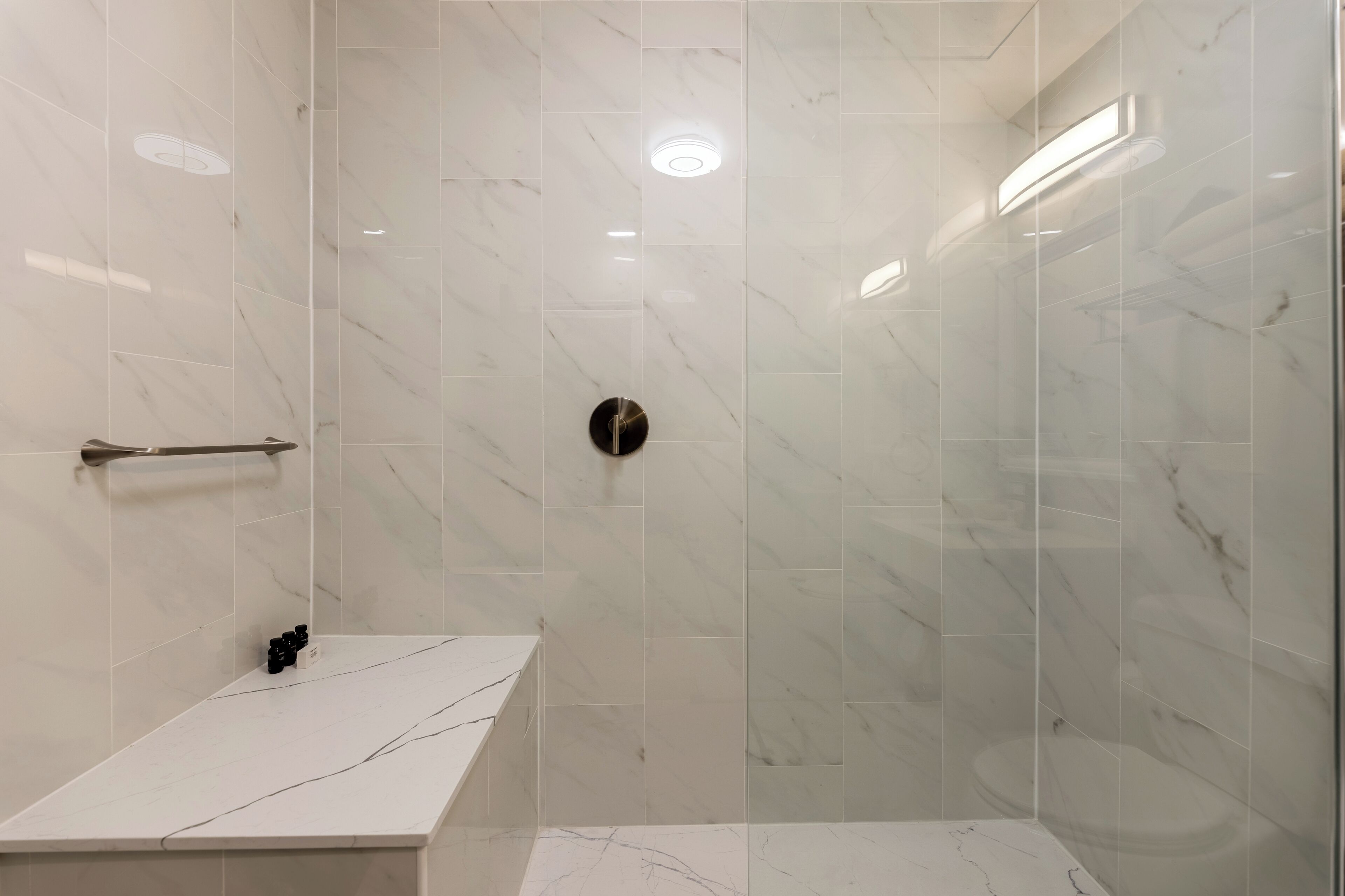 Un baño moderno con tocador de mármol, cabina de ducha de vidrio y un secamanos visible.
