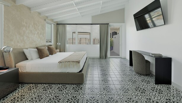 A modern hotel room with a large bed, a desk, a TV, and a view of the city through the window. - Hotel Milano (San Juan)
