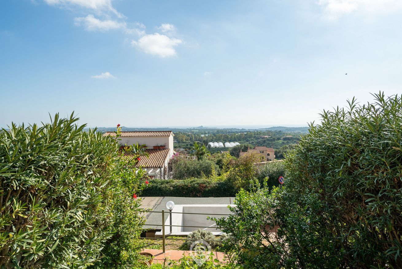 A villa with a tiled roof, surrounded by lush greenery and a clear view of the countryside.