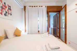 A bedroom with a bed, white curtains, a wooden door, and a view of the outdoors.