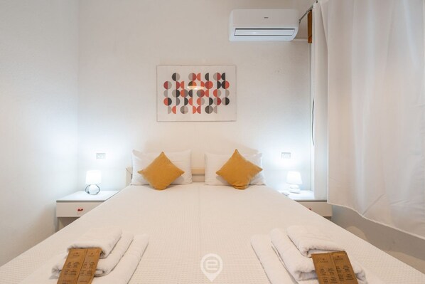 A hotel room with a large bed, two nightstands, a wall-mounted air conditioner, and a decorative wall piece.
