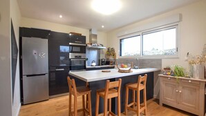 A modern kitchen with a central island, wooden chairs, a refrigerator, and a window providing natural light. - 3 bedroom gorgeous home in Amfreville (Amfreville)