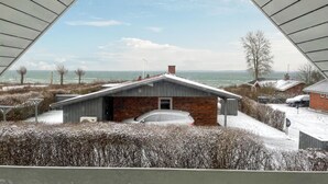 A modern house with a brick facade and a sloped roof, situated in a snowy landscape with a view of the ocean. - 3 bedroom gorgeous home in Hesselager (Hesselager)