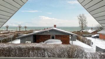 A modern house with a brick facade and a sloped roof, situated in a snowy landscape with a view of the ocean.