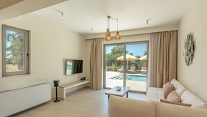 A modern living room with a sofa, a coffee table, and a TV on a stand. There is a window with curtains, a radiator, and a pool visible through the glass doors. - 200m to the beach | brand new 2024 | Villa Erato - Elysian Villas (Kefalonia)