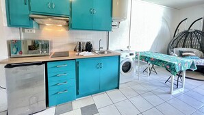 Eine kompakte Küche mit türkisfarbenen Schränken, einer Mikrowelle, einer Kaffeemaschine und einer Waschmaschine.