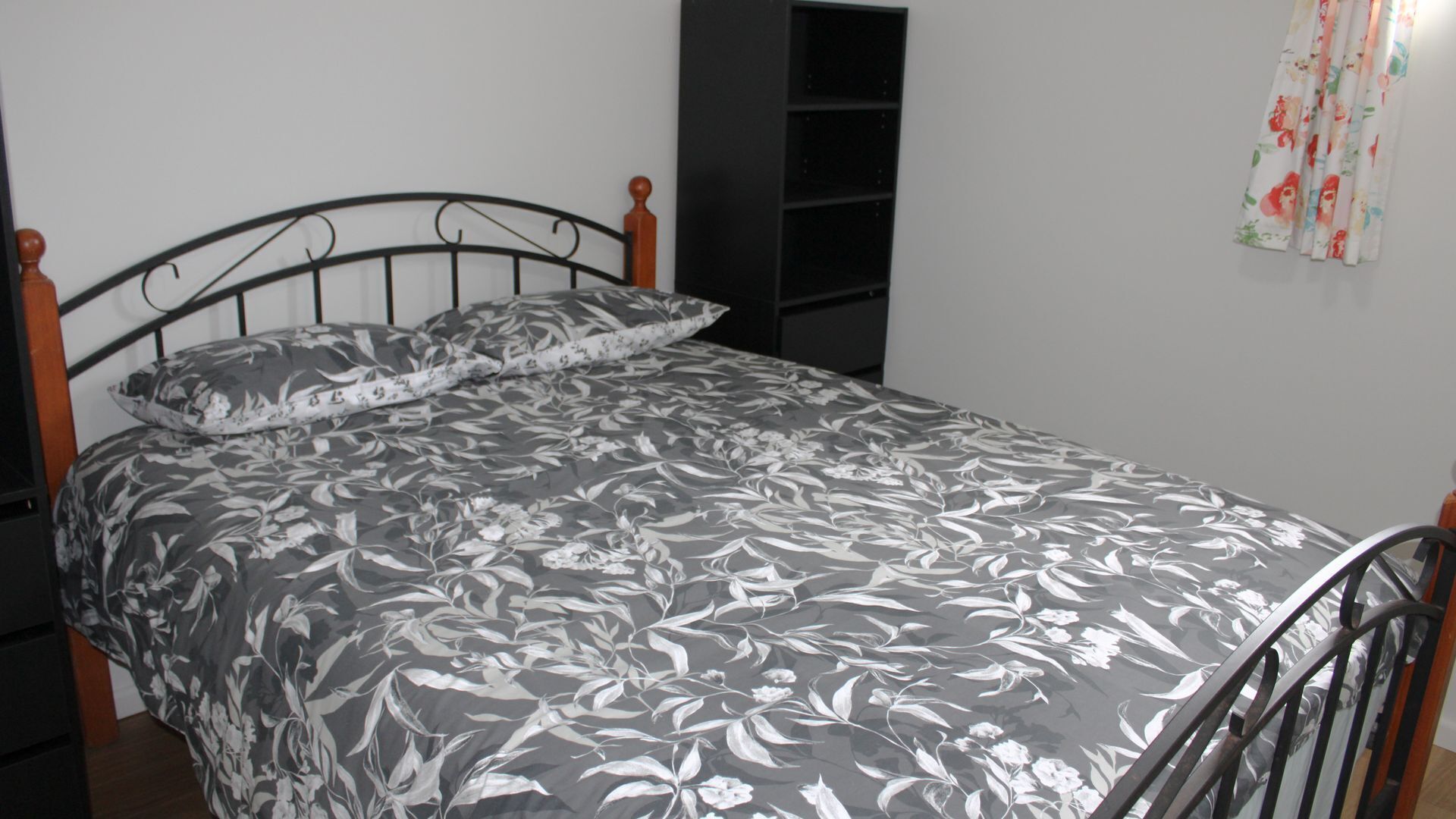 Una cama con colcha estampada de flores, cabecera de madera y estructura de metal negro.