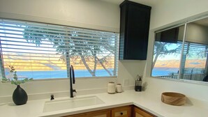 A kitchen with wooden cabinets, a white countertop, a sink, and a window with blinds.