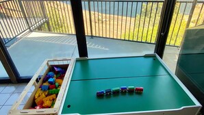 A pool table with colorful toy cars and a toy car box on a balcony with a scenic mountain and lake view.