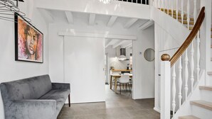 Un intérieur moderne avec un canapé gris, un escalier doté de balustrades blanches et un coin repas à l’arrière-plan.
