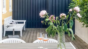 Une terrasse avec une table dressée pour deux personnes, un banc blanc et un vase rempli de fleurs.