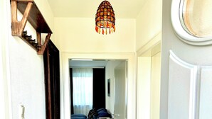 Een gang met een zwarte betegelde vloer, een houten plank met een spiegel, een hanglamp en een bed op de achtergrond.