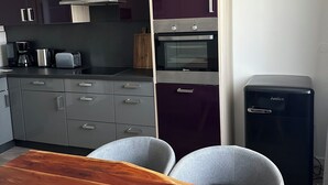 Een moderne keuken met grijze kastjes, een ingebouwde oven, een koffiezetapparaat en een kleine koelkast.
