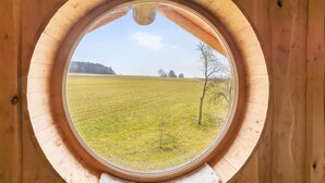 A circular wooden window with a view of a grassy field and a tree. - Awesome home in Waffenbrunn with sauna (Waffenbrunn)