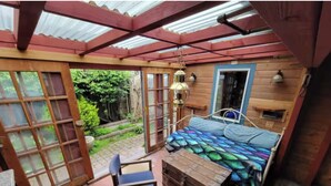Une pièce confortable avec un lit, une petite table et une chaise. Il y a une fenêtre et une porte qui donne sur l’extérieur.