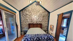 Une chambre avec un mur en pierre, un lit recouvert d’une couvre-lit à motifs et une porte en bois.
