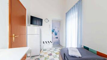 A compact hotel room with a bed, a desk, a refrigerator, a television, and a bathroom visible through an open door.