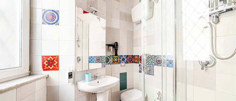 A bathroom with a white sink, toilet, and shower. The walls are tiled with colorful patterns.