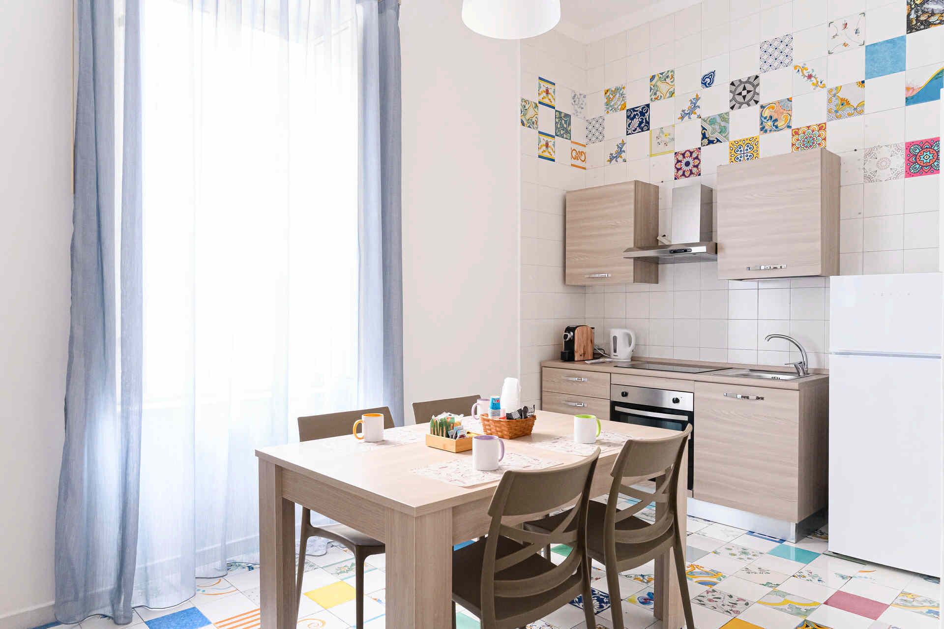 Una cocina moderna con armarios de madera, una mesa de comedor con sillas y baldosas de suelo coloridas.
