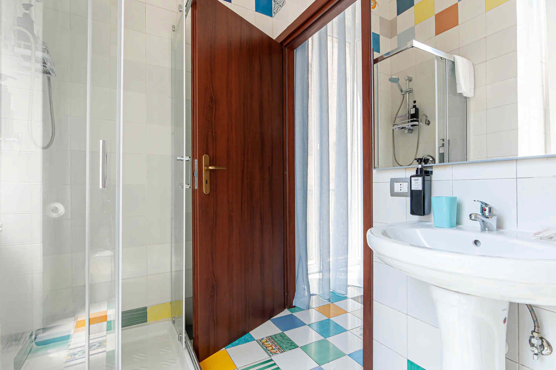 A bathroom with a shower, a sink, a mirror, and a door.