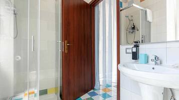 A bathroom with a shower, a sink, a mirror, and a door.