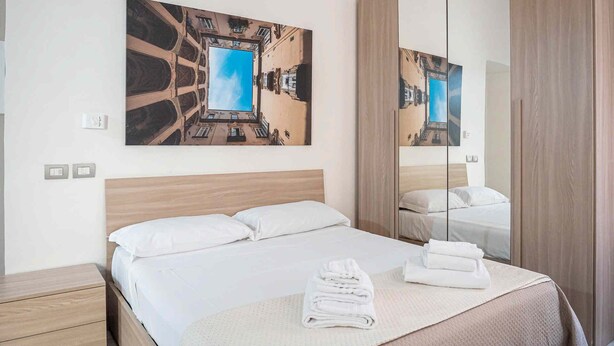 A hotel room with a bed, a large mirror, and a painting of a building. - La Dimora Di Parthenope (Naples)