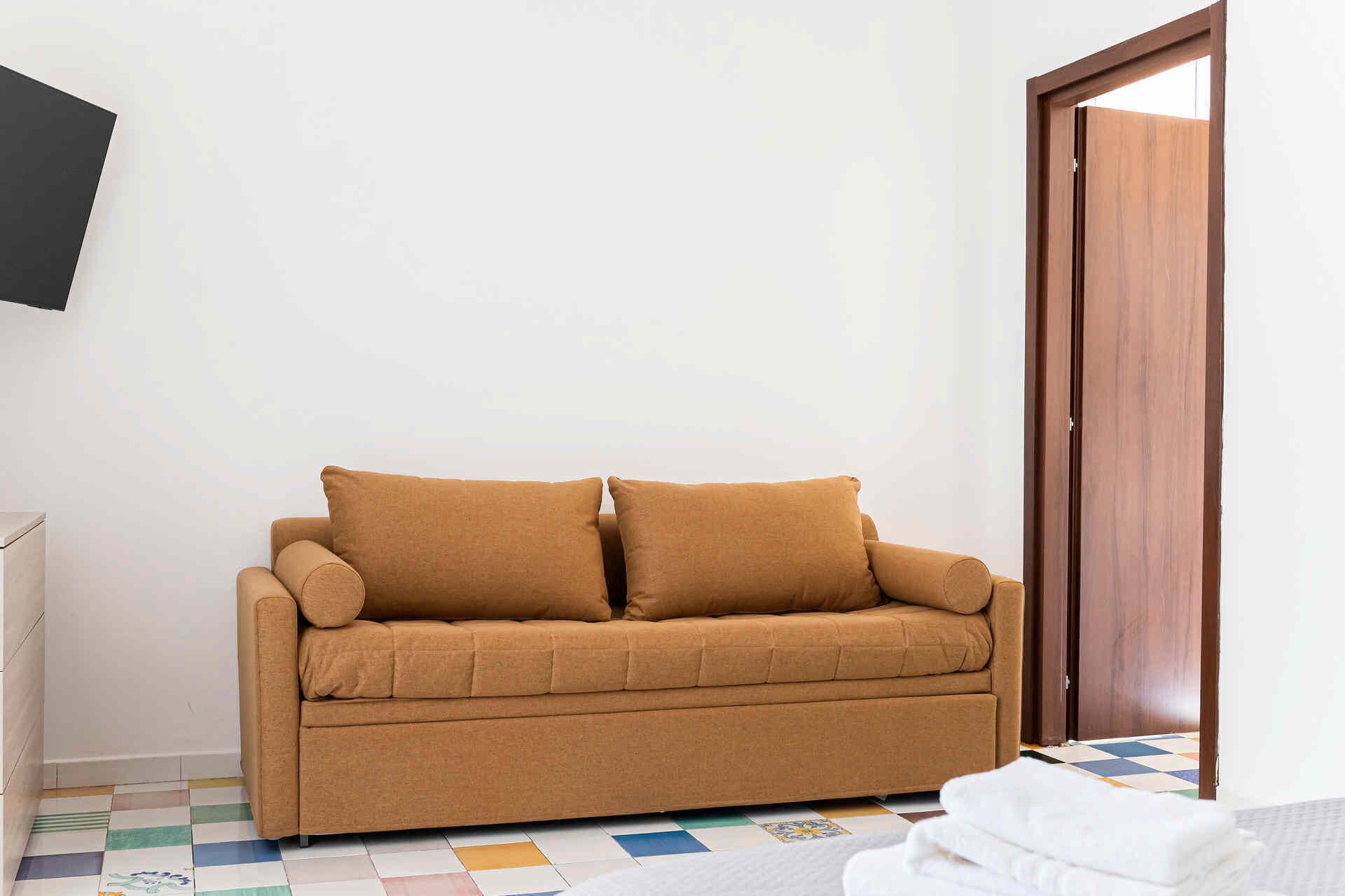 A room with a brown sofa, a wooden door, and a tiled floor.