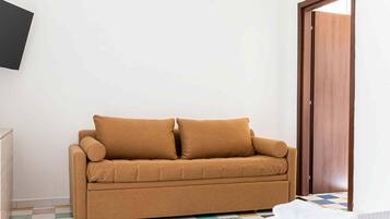 A room with a brown sofa, a wooden door, and a tiled floor.