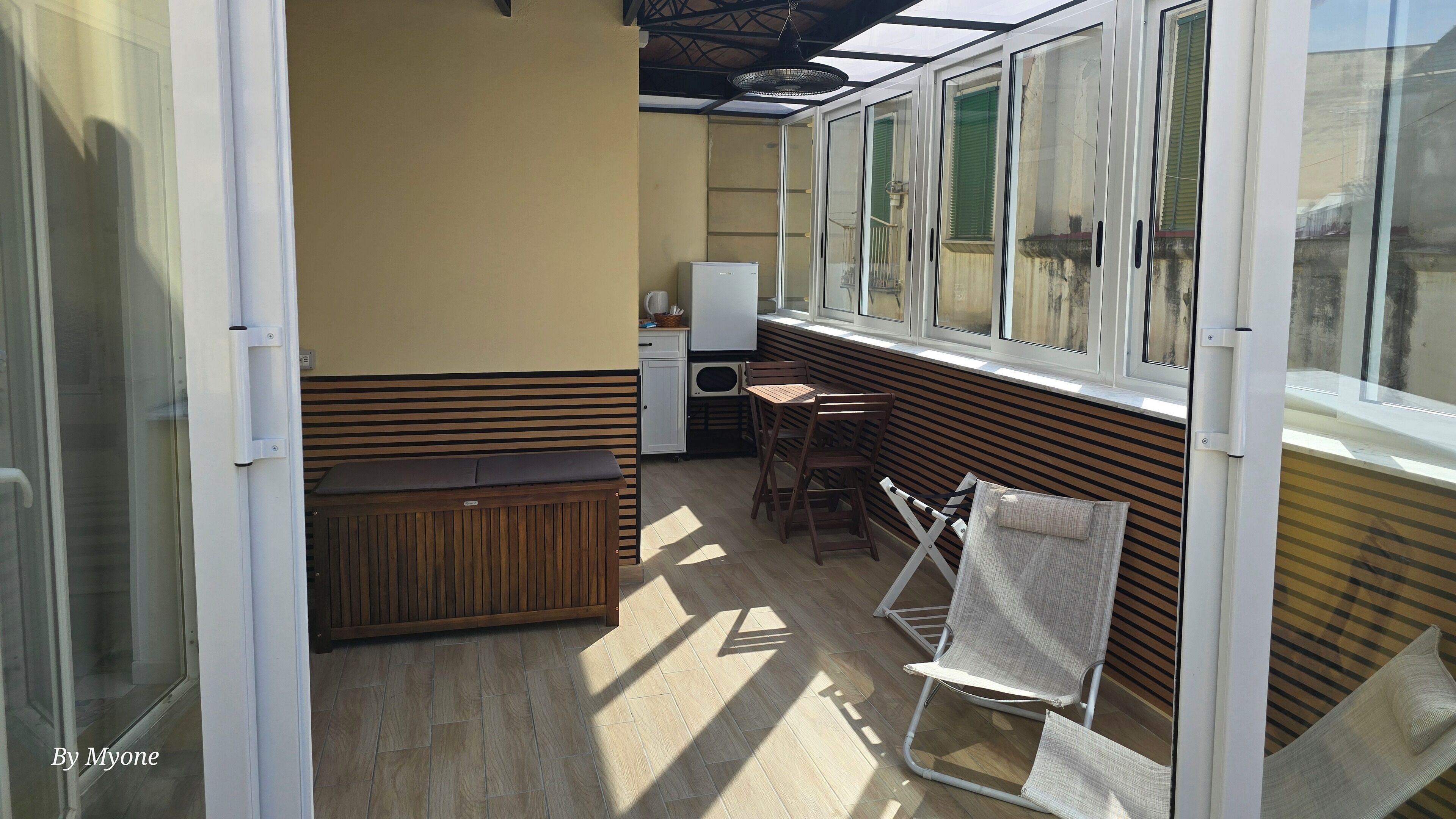 Una habitación luminosa con un banco de madera, una mesa con sillas y un refrigerador.