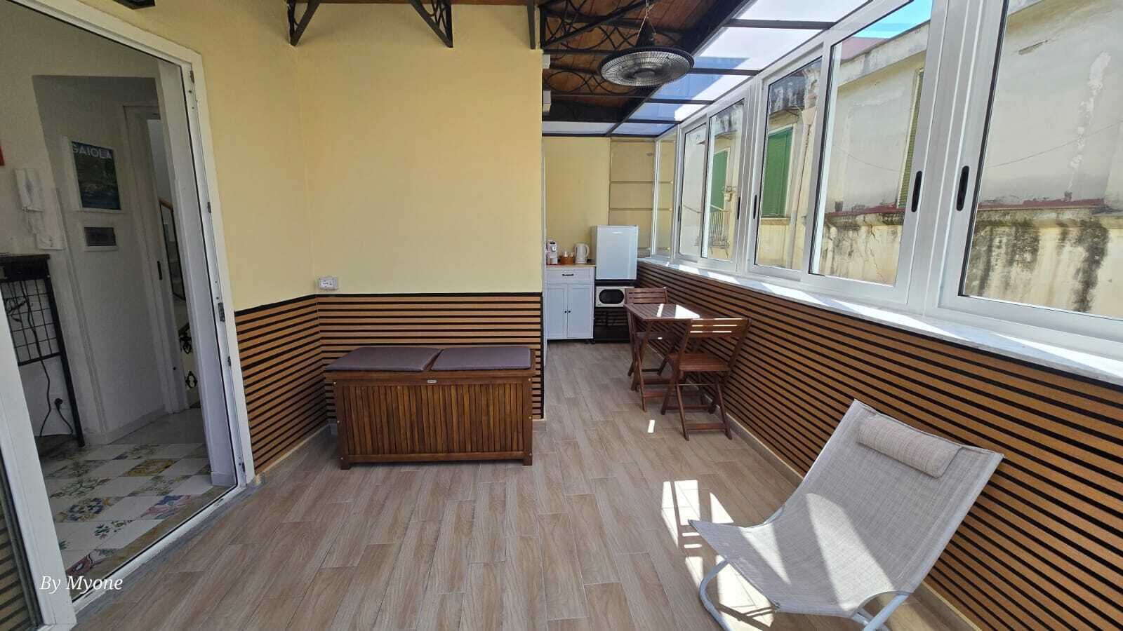 A sunlit room with a wooden bench, a small table with chairs, and a refrigerator.