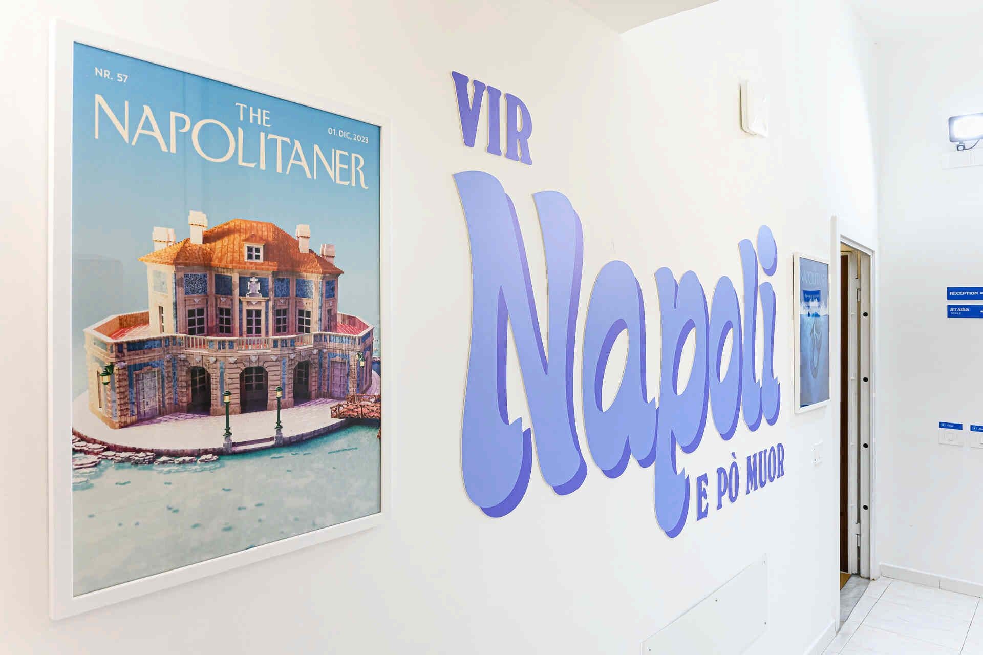 Eine Wand mit einem gerahmten Poster eines Gebäudes und dem Text 'VIR Napoli E PÒ MUOR'.