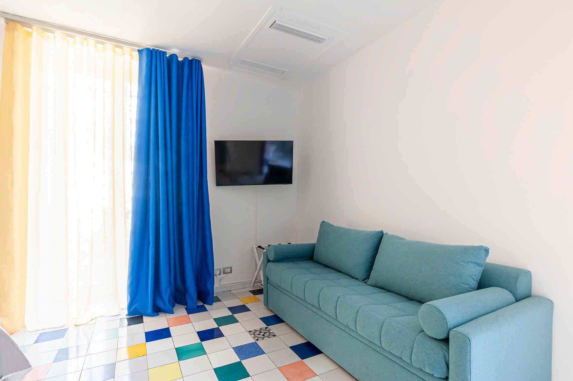 Een kamer met een smaragdgroene bank, een aan de muur bevestigde televisie en een geruite vloer.