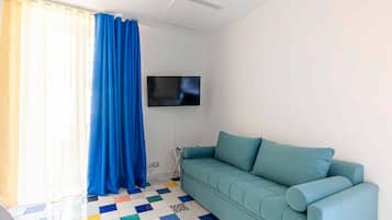 Una habitación con un sofá color turquesa, un televisor montado en la pared y un suelo a cuadros.