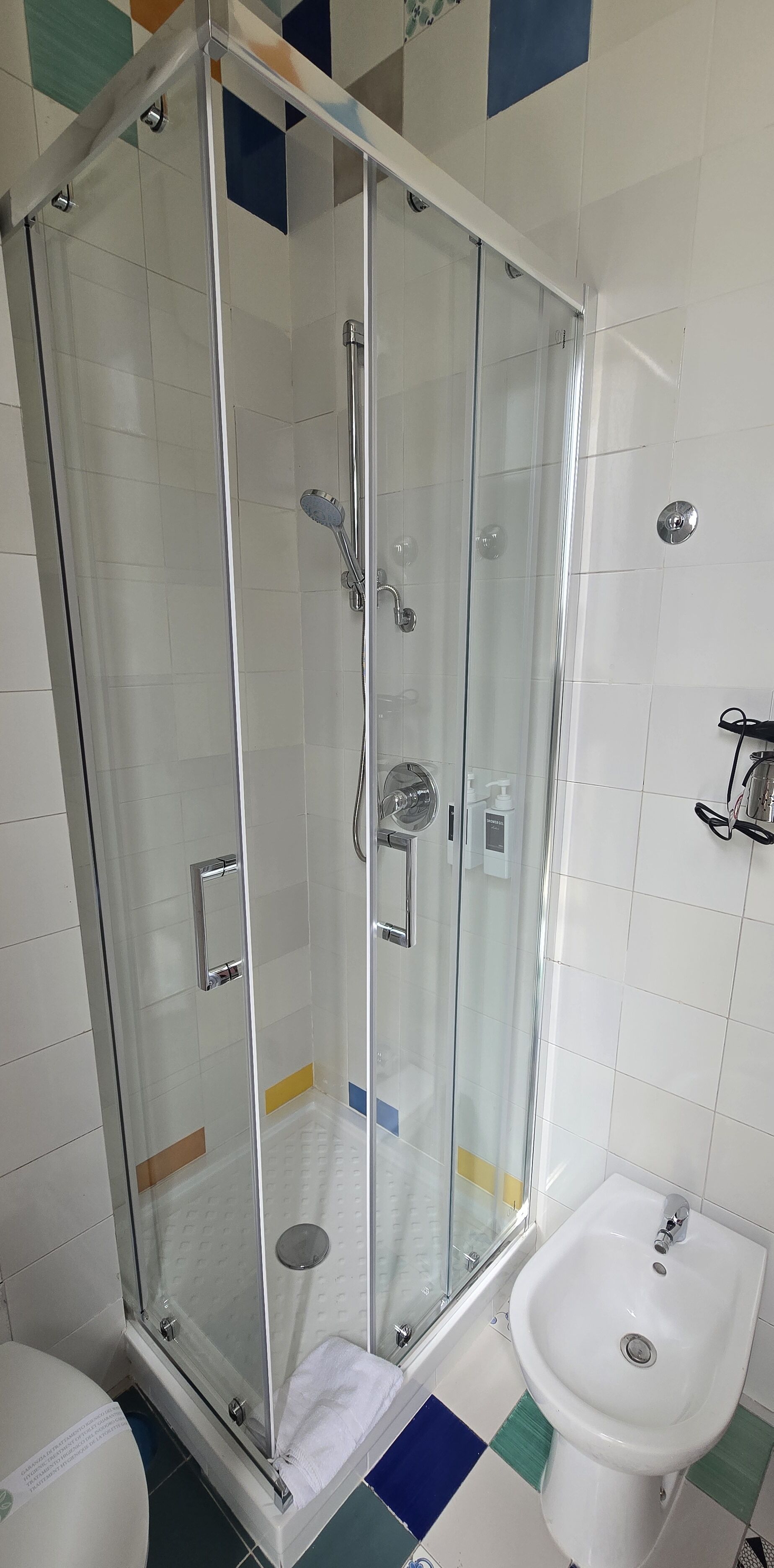 Ducha envuelta en vidrio con un cabezal de ducha manual, otro cabezal de ducha manual y un grifo empotrado.