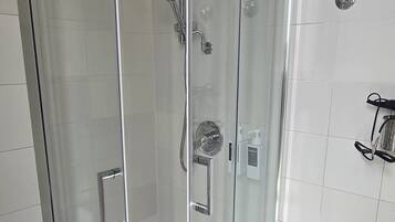 Ducha envuelta en vidrio con un cabezal de ducha manual, otro cabezal de ducha manual y un grifo empotrado.