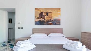 Camera d'albergo con un letto grande, due cuscini, una testiera, un comodino, un termosifone, un quadro appeso alla parete e vista su un castello sul mare.